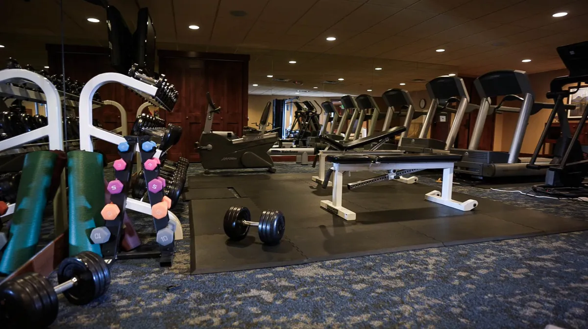 This image features a well-equipped fitness center with treadmills, dumbbells, a weight bench, and various exercise machines. The space is bright, open, and motivational, inviting guests to enjoy a workout or participate in group classes.