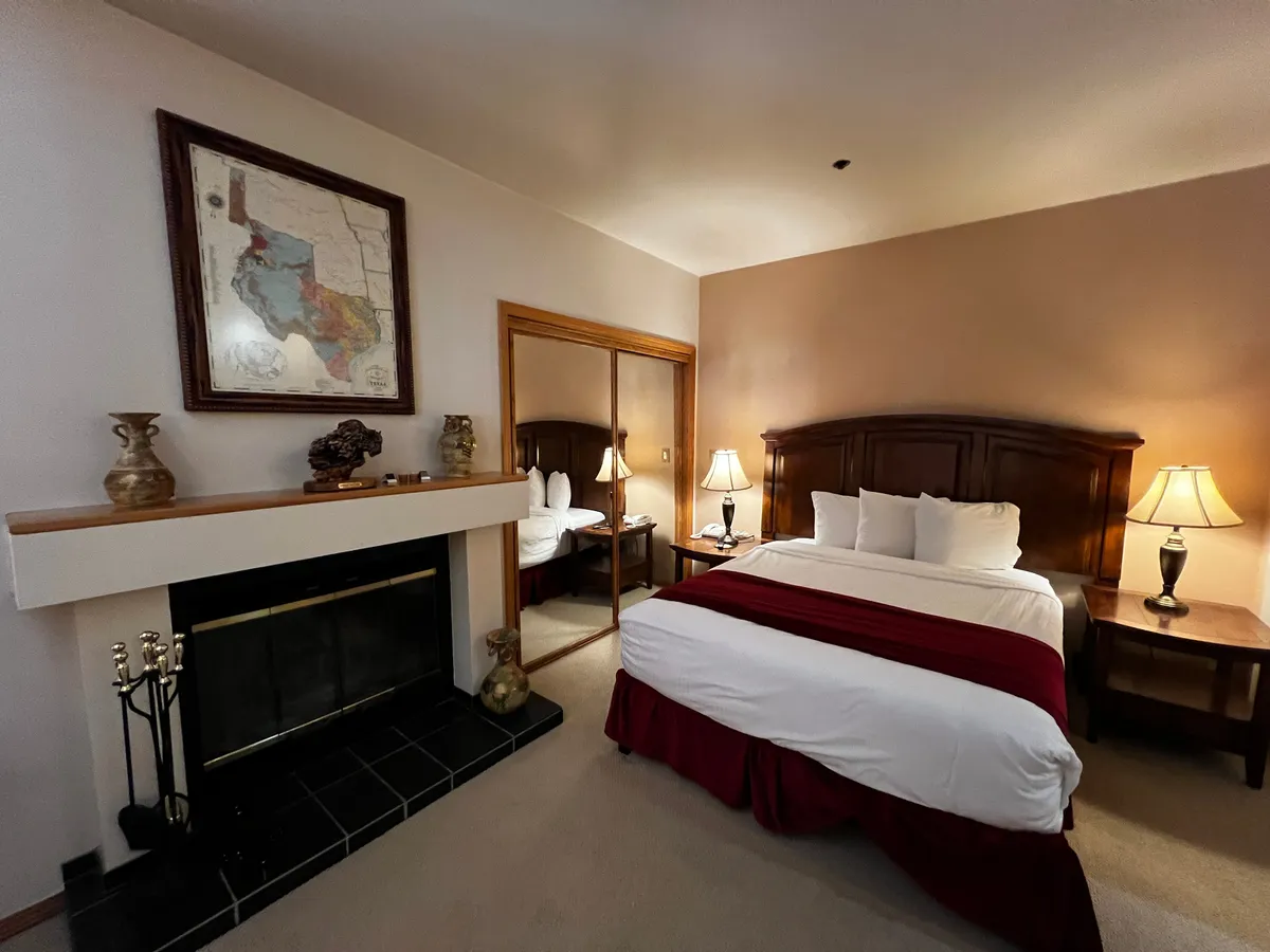 A stylish bedroom scene with a bed featuring a red accent, a rustic fireplace for added warmth, wooden furnishings, artistic décor including a framed map, and decorative vases. The room radiates an inviting and cozy ambiance, ideal for restful nights and intimate evenings.
