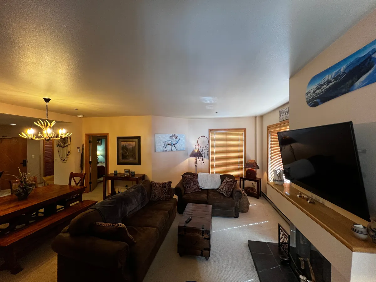 An inviting living/dining area with a comfortable sofa, wooden dining table, TV, and wall art. Soft lighting and natural textures create a cozy atmosphere, making the space ideal for both quiet moments and lively gatherings.